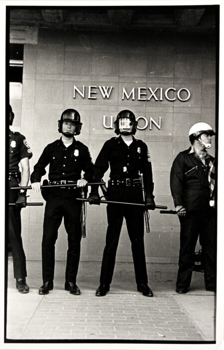 Police officers stand in a line outside the Student Union, holding batons out.