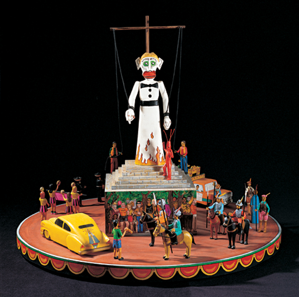 Colorful diorama of the puppet, Zozobra, and fiesta-goers surrounding him. The figurines are arranged on an orange circular base. A yellow car appears at the base of the Zozobra figure, along with people on horses.